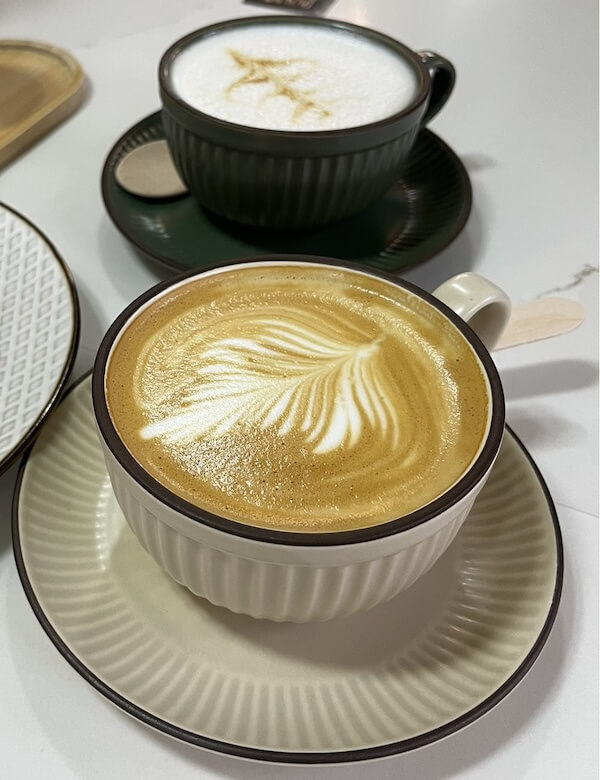 Zwei Tassen Kaffee stehen auf einem Tisch. Die eine Tasse ist Beige und die andere schwarz.